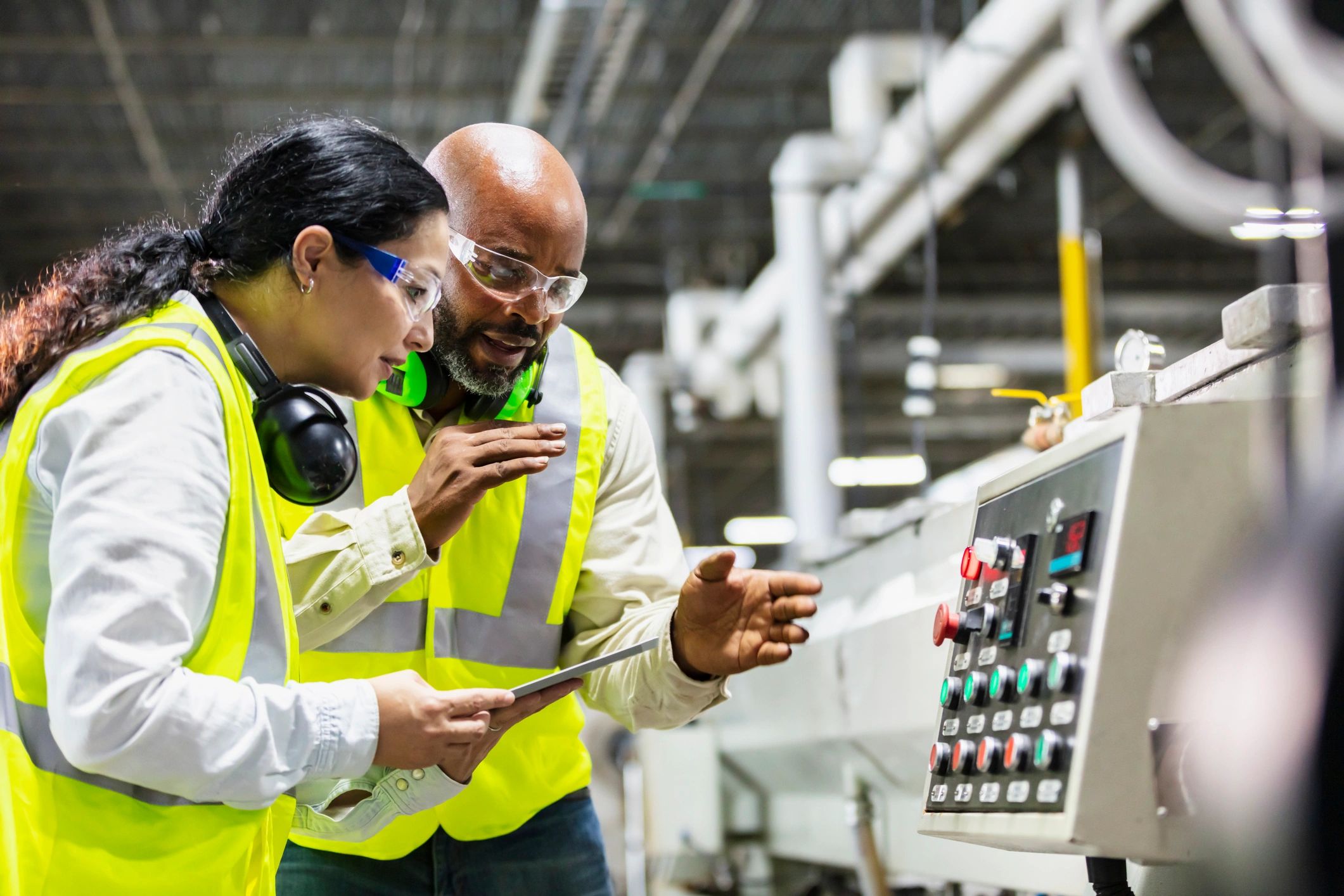 Two factory workers reviewing a machine control panel